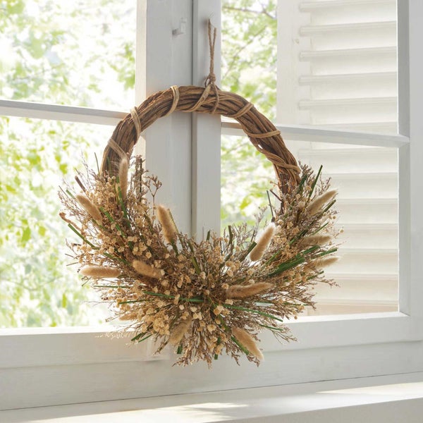 Dekorativer Kranz aus Trockenblumen und Gräsern, hängend an einem weißen Fensterrahmen.