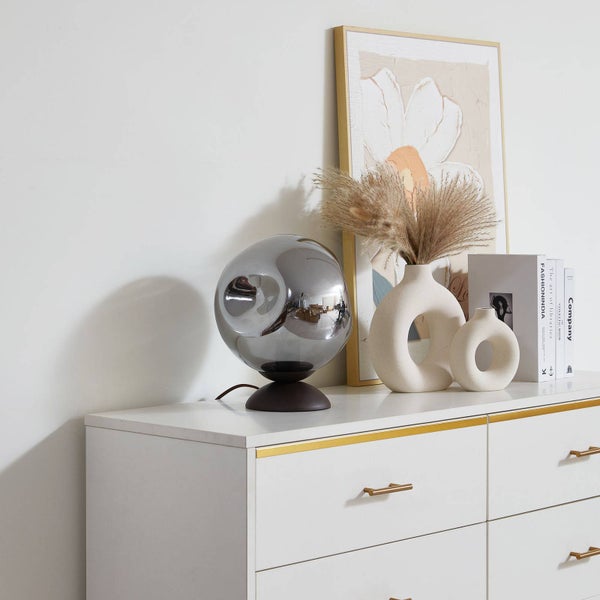 Dekorative Szene mit einer silberfarbenen Kugel-Tischlampe, zwei Vasen und Büchern auf einer Kommode