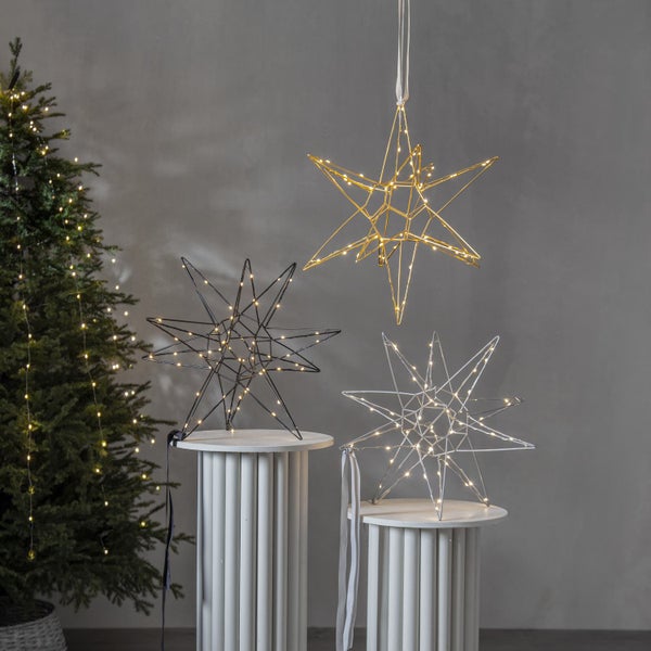 Dekorative Sternleuchten in Gold, Silber und Schwarz auf Säulen mit beleuchtetem Weihnachtsbaum
