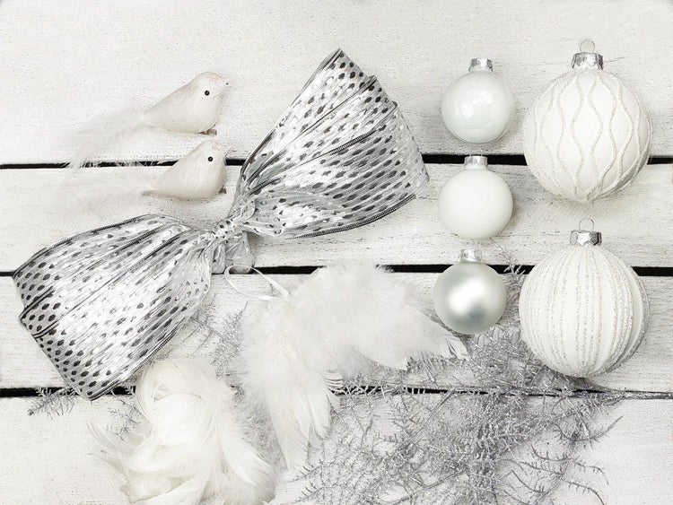 Set mit silbernen Weihnachtskugeln, einer großen Schleife, Deko Vögeln, Federflügeln und glitzernden Zweigen als Weihnachtsdekoration.