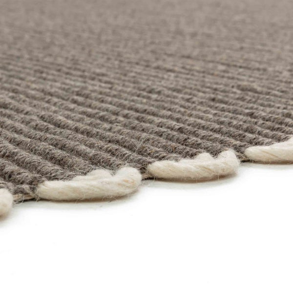 Nahaufnahme eines grauen Teppichs mit Rippenstruktur und weißen Schlaufen am Rand.