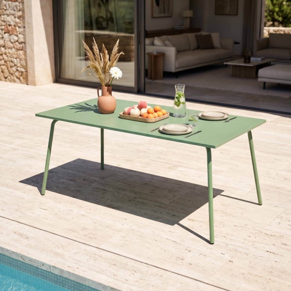 Moderner, rechteckiger Gartentisch aus grünem Metall auf einer hellen Terrasse am Pool, dekoriert mit Geschirr, Obst und Trockenblumen.