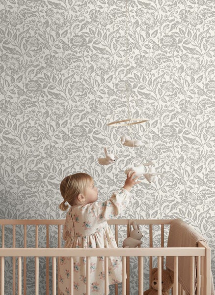 Vliestapete mit floralem Muster in einem hellen Kinderzimmer hinter einem Gitterbett aus Holz mit einem Mobile.