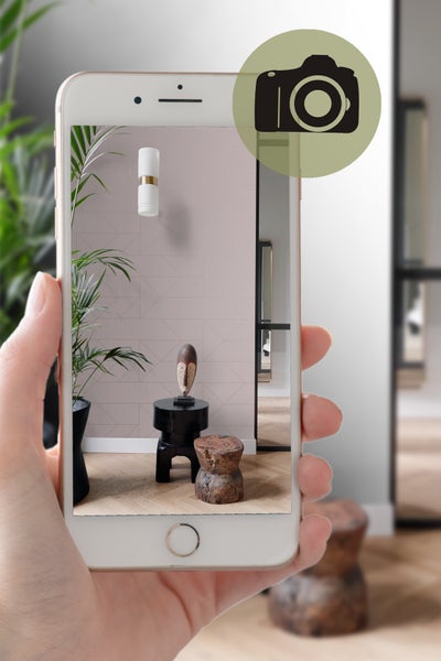 Aufnahme eines Raumes mit geometrischer Tapete, einer Wandleuchte, Pflanzen und dekorativen Hockern, aufgenommen mit einem Smartphone.