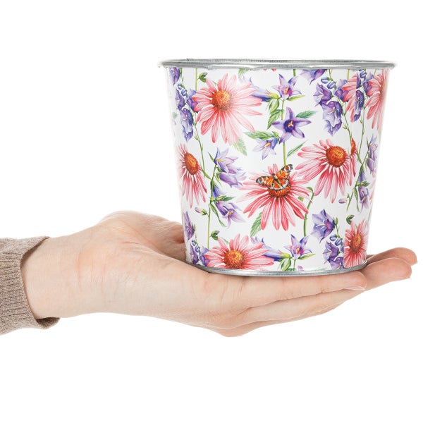 Blumenübertopf aus Metall mit floralem Dekor aus Sonnenhut, Glockenblumen und Schmetterling, in einer Hand gehalten.
