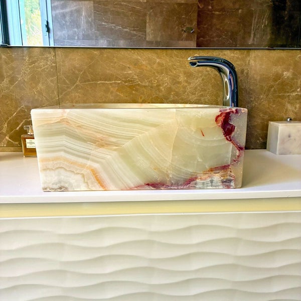 Rechteckiges Aufsatzwaschbecken aus Naturstein mit markanter Maserung auf einem weißen Unterschrank mit Wellenstruktur und einer Chromarmatur.