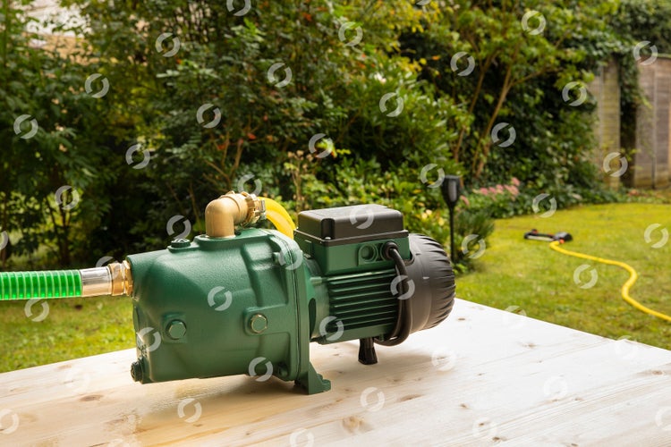 Grüne Gartenpumpe auf einem Holztisch in einem Garten mit angeschlossenem grünem Saugschlauch und gelbem Gartenschlauch.