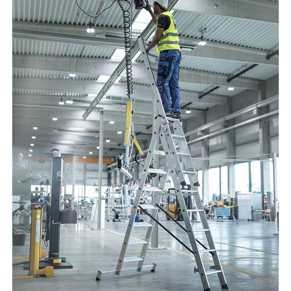 Eine Person steht auf einer Aluminium-Stufenleiter in einer Industriehalle.