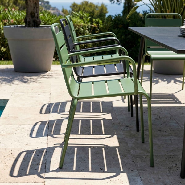 Moderne Gartenstühle aus Metall in Grün und Schwarz an einem dunklen Gartentisch auf einer hellen Steinterrasse mit Pflanzkübel.