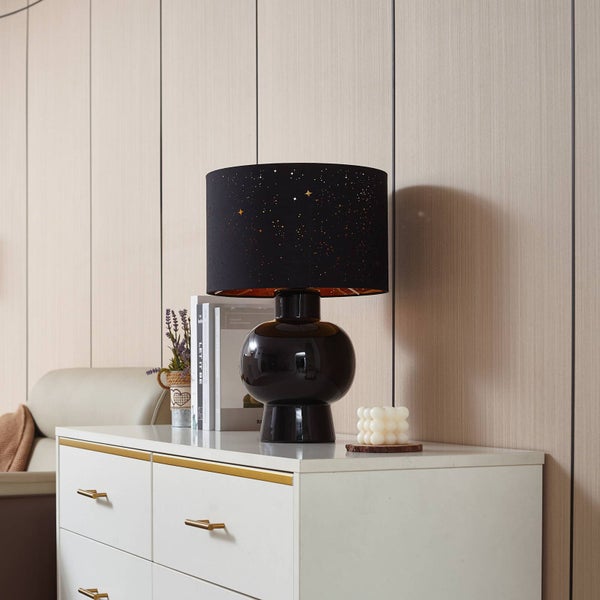 Schwarze Tischleuchte mit Sternenmuster auf einem Nachttisch