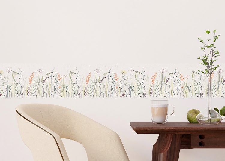 Bordüre mit Wildblumen-Wiesenmuster an einer hellen Wand in einem minimalistischen Raum mit Sessel und Beistelltisch.