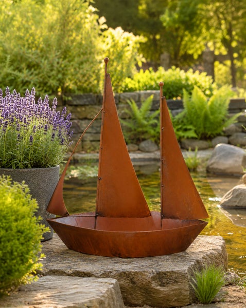 Dekoratives Segelschiff aus Metall mit Edelrost Patina als Gartenfigur am Teichrand platziert.