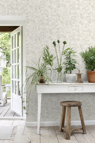 Dekoratives Interieur mit gemusterter Tapete, Tisch, Pflanzen und Hocker