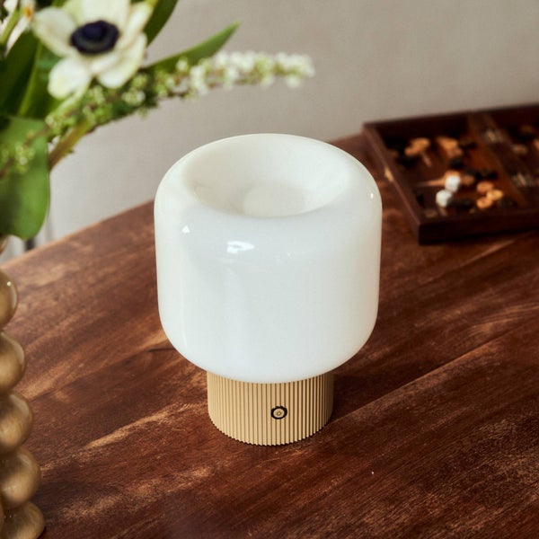 Moderne Tischleuchte mit weißem, abgerundetem Schirm und geriffeltem Holzfuß auf einem dunklen Holztisch.