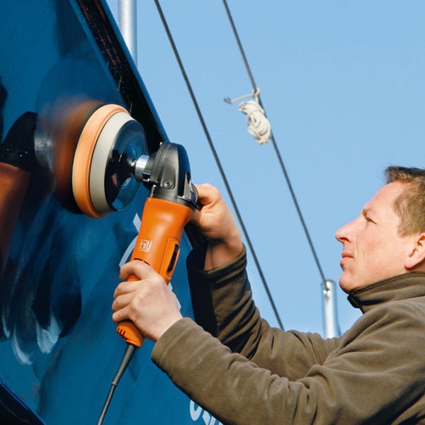 Ein Mann verwendet eine FEIN Poliermaschine zur Bearbeitung einer dunklen Oberfläche an einem Boot im Freien.