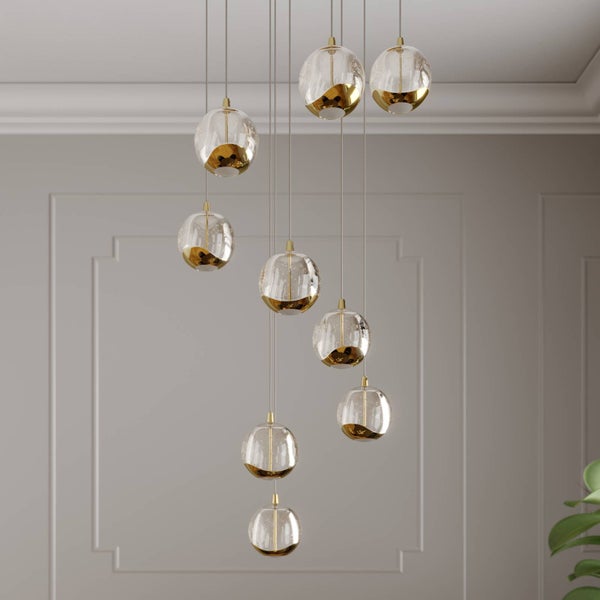 Moderne Pendelleuchte mit neun runden Glasschirmen in unterschiedlichen Höhen. Klare Glaskugeln mit goldfarbenen Details an schmalen Kabeln.