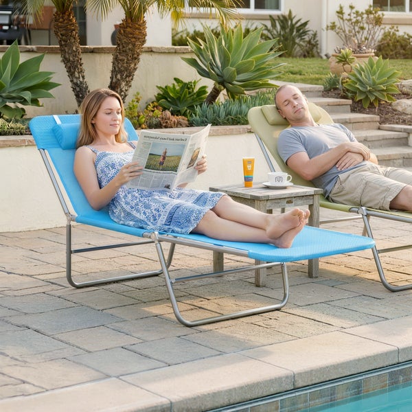 Eine Frau und ein Mann entspannen auf Gartenliegen auf einer Steinterrasse an einem Pool, umgeben von grünen Gartenpflanzen.