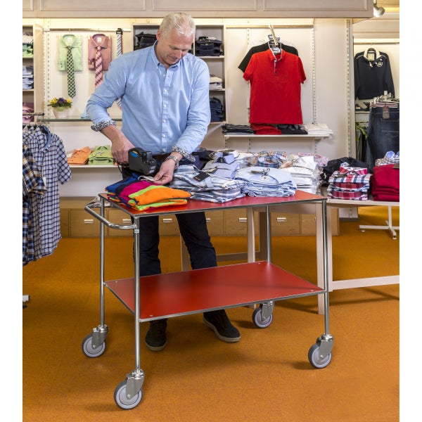 Szene in einem Bekleidungsgeschäft mit einem Mitarbeiter, der einen Scanner an einem Kleiderwagen mit gestapelter Kleidung verwendet.