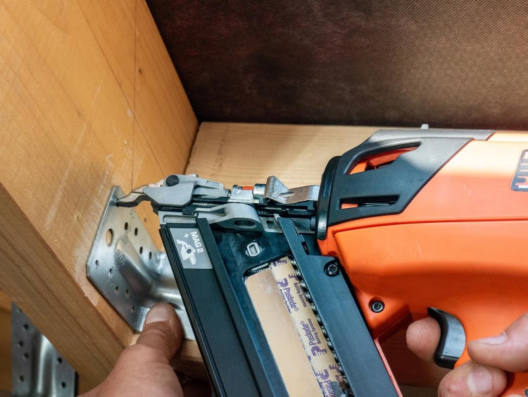Ein akkubetriebener Nagelgerat von Paslode beim Befestigen eines Metallwinkels an einer Holzbalkenkonstruktion.