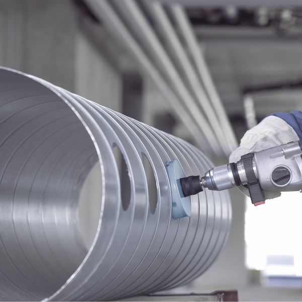 Eine Person verwendet eine Bohrmaschine mit Schleifscheibe, um ein Metallrohr zu bearbeiten.