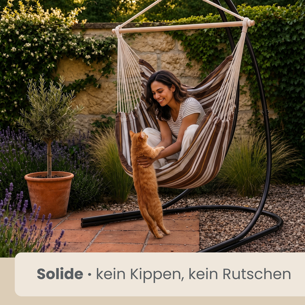 Frau entspannt in einem gestreiften Hängesessel mit Metallgestell im Garten, während eine Katze vor ihr steht.