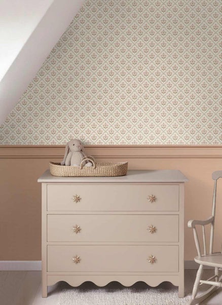 Kinderzimmer mit floral gemusterter Tapete, beiger Kommode mit Sternengriffen und einem Korb mit Stofftier in warmen Farbtönen.