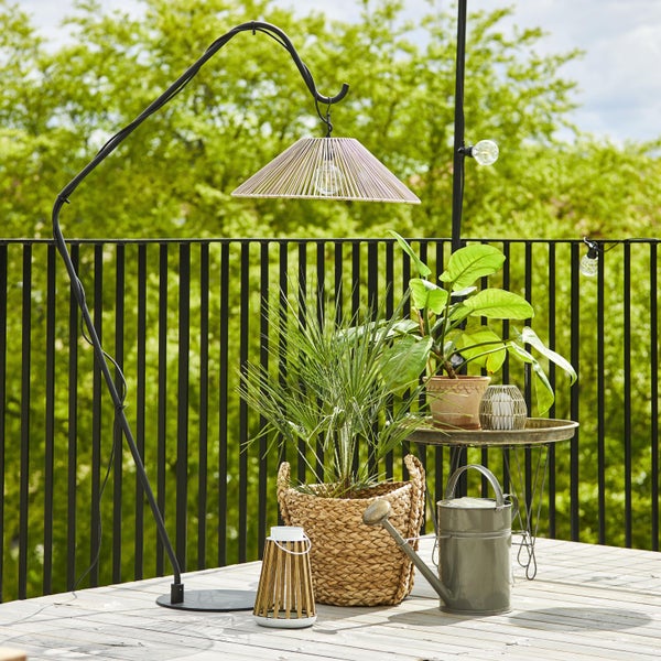 Dekorative Gartenszene mit Stehlampe, Pflanzen, Gießkanne und Laterne auf einer Holzterrasse.