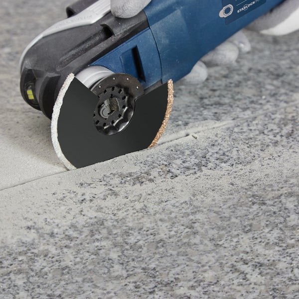 Detailaufnahme eines Multitools beim Entfernen von Fugen zwischen Fliesen.