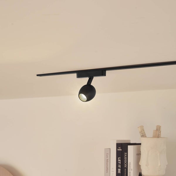 Schwarzer, runder Strahler für ein Schienensystem an der Decke montiert.