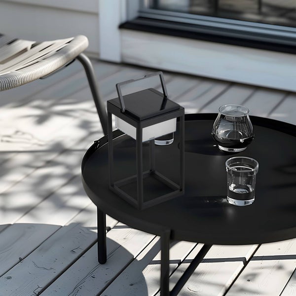 Schwarze, quadratische Solarlaterne auf einem runden schwarzen Beistelltisch auf einer hellen Holzterrasse.
