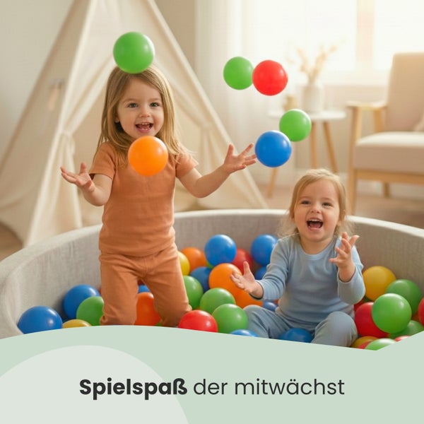 Zwei Kinder spielen in einem Bällebad mit bunten Kunststoffbällen in einem hellen Zimmer mit Tipi-Zelt.