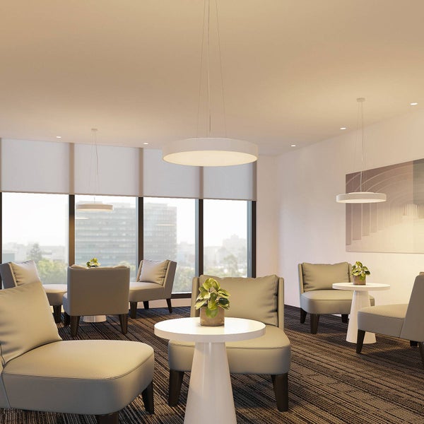 Moderner Büroraum mit runden LED-Pendelleuchten, grauen Polstersesseln und weißen Beistelltischen mit grünen Pflanzen.