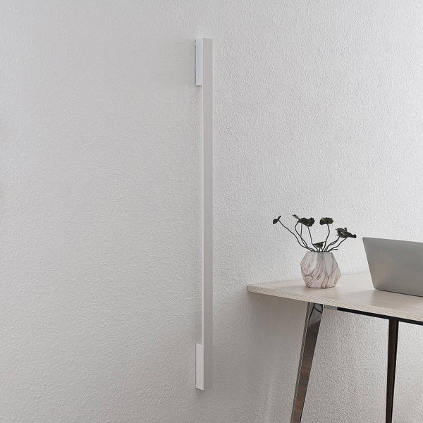 Lange schlanke LED-Wandleuchte vertikal an einer weissen Wand neben einem Schreibtisch montiert.