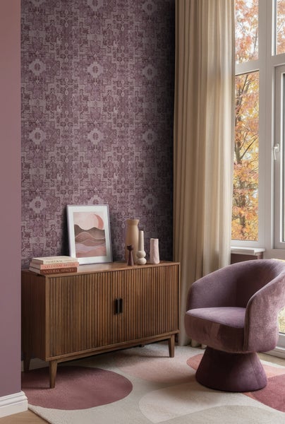 Modernes Wohnzimmer mit gemusterter Tapete in Lila, einem Sideboard aus Holz mit Deko, einem Sessel und einem Fenster mit Herbstblick.