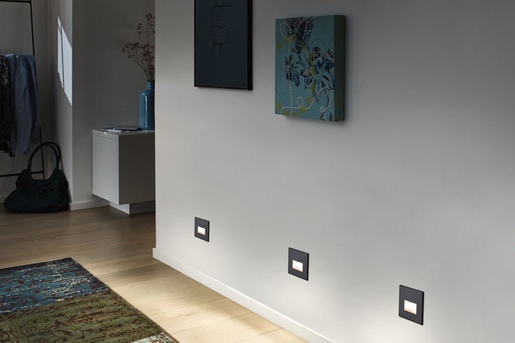 Moderne Flurszene mit drei quadratischen LED-Wandeinbauleuchten, die bodennah an einer Wand montiert sind und warmes Orientierungslicht spenden.