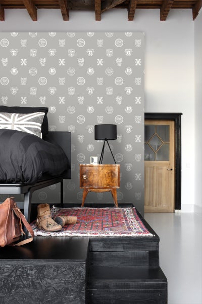 Schlafzimmer mit Bett, Nachttisch, Lampe und gemusterter Tapete