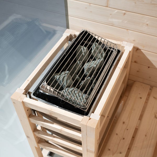 Saunaofen mit Saunasteinen in einer Holzverkleidung aus hellem Holz in einer Sauna mit Holzwänden.