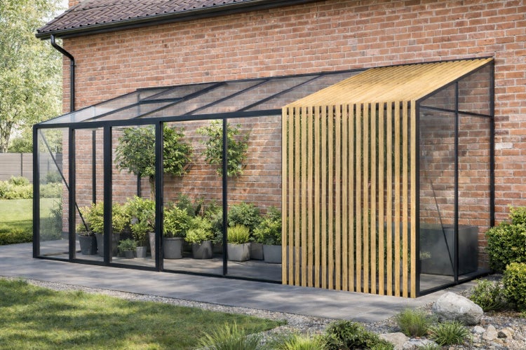 Modernes Anlehngewächshaus mit schwarzem Metallrahmen, Glaselementen und Sichtschutz aus Holzlamellen an einer Ziegelwand im Garten.