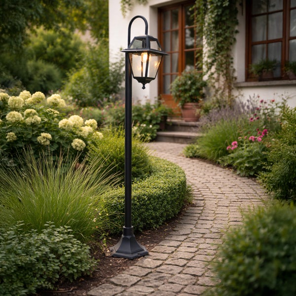 Traditionelle schwarze Gartenlaterne aus Metall an einem gepflasterten Gartenweg mit blühenden Pflanzen und Sträuchern.