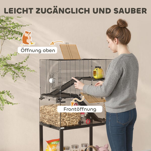 Eine Frau demonstriert den Zugang zu einem mehrstöckigen Kleintierkäfig mit oberer Klappe und Frontöffnung. Beinhaltet Rampe, Laufrad und Einstreu.