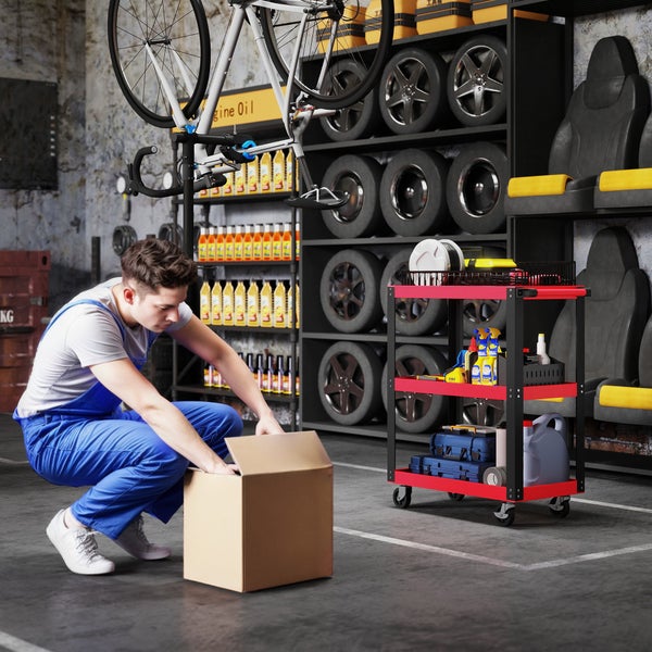Werkstatt mit Regalen voller Reifen und Autozubehör, ein Mechaniker hockt vor einem Karton