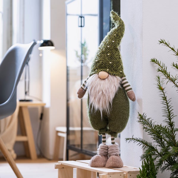 Dekorativer Weihnachtswichtel mit Bart und Mütze steht auf einem Holzpodest