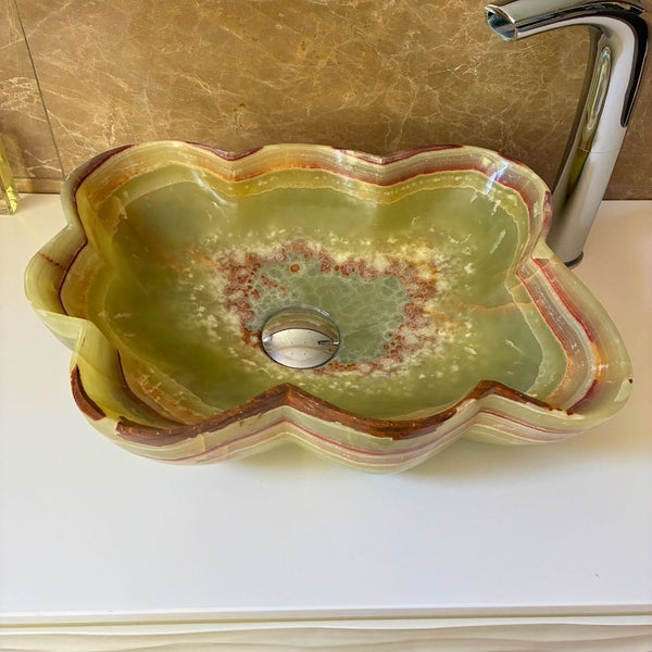 Wellenförmiges Aufsatzwaschbecken aus Onyx-Naturstein mit Armatur auf einem Waschtisch.