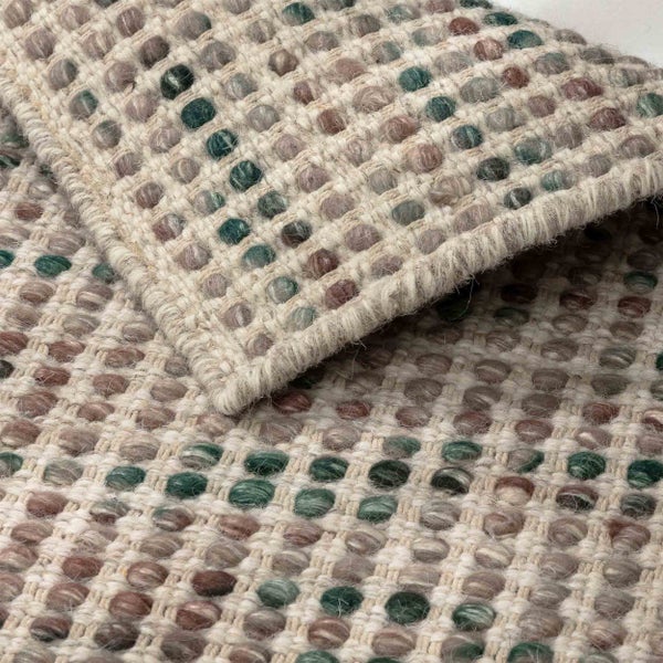 Nahaufnahme eines gewebten Teppichs mit einem erhabenen Noppenmuster in verschiedenen Farben und einer umgeschlagenen Ecke.