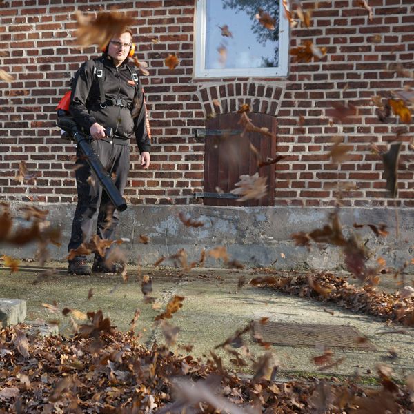 Mann benutzt Laubbläser zum Entfernen von Blättern vor einem Haus.