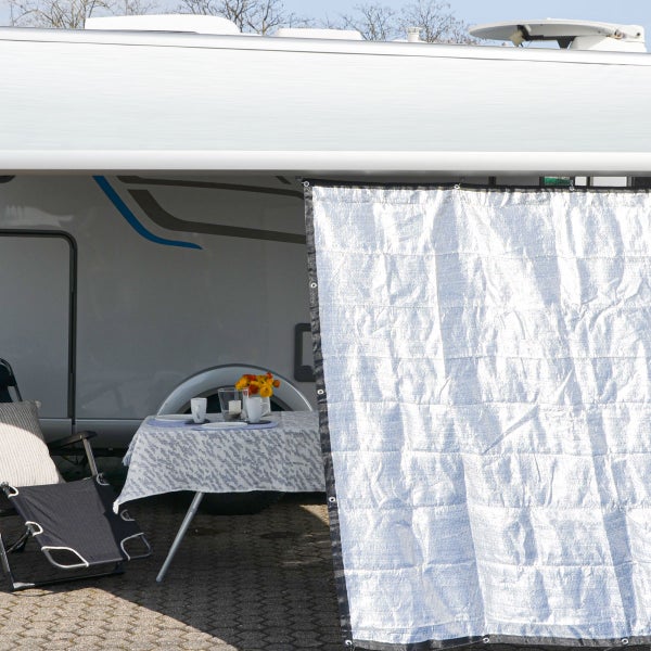 Silberne reflektierende Thermomatte als Seitenwand an einem hellen Wohnmobil befestigt, bietet Hitze- und Sonnenschutz für Campingtisch und Stuhl.