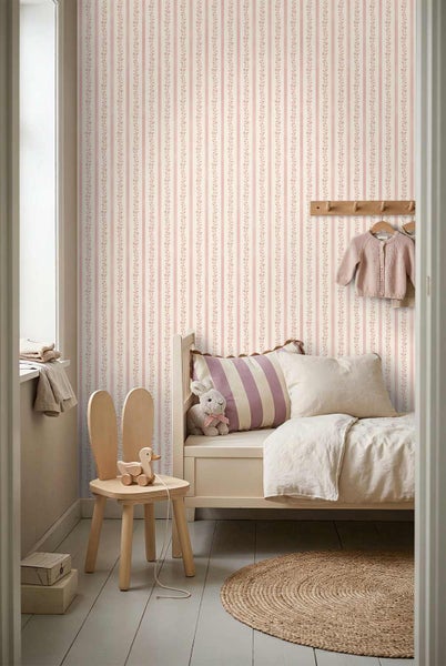 Kinderzimmer mit gestreifter Blumentapete, Holzbett, Hasenohren-Stuhl und rundem Juteteppich. Hell und strukturiert gestaltet.
