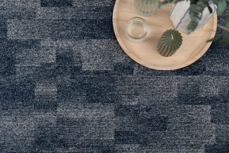 Gemusterter Teppich mit strukturierter Oberfläche und einem runden Holztablett mit Dekoration.