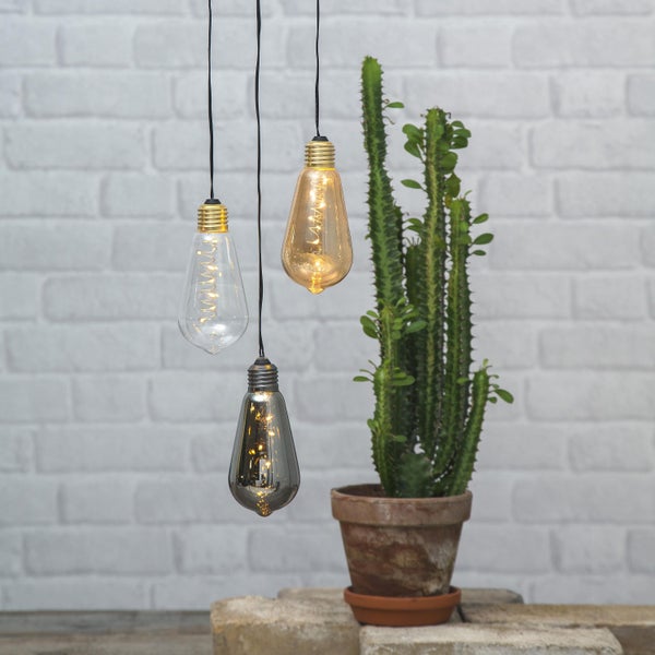 Drei hängende Glühbirnen und ein Kaktus in einem Topf vor einer Ziegelwand