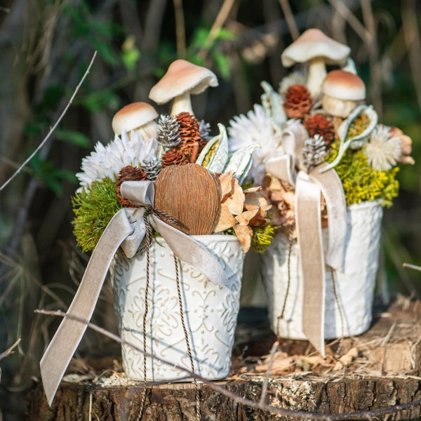 Zwei dekorative Gestecke mit Pilzen, Zapfen und Schleife in verzierten Töpfen